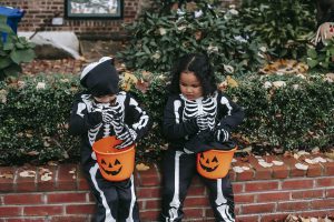 Children in skeleton costumes sitting on brick wall which borders a garden